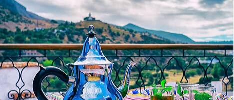 Ein Tisch mit Teekanne, Gläsern und einer gestreiften Decke auf einem Balkon mit Bergblick.