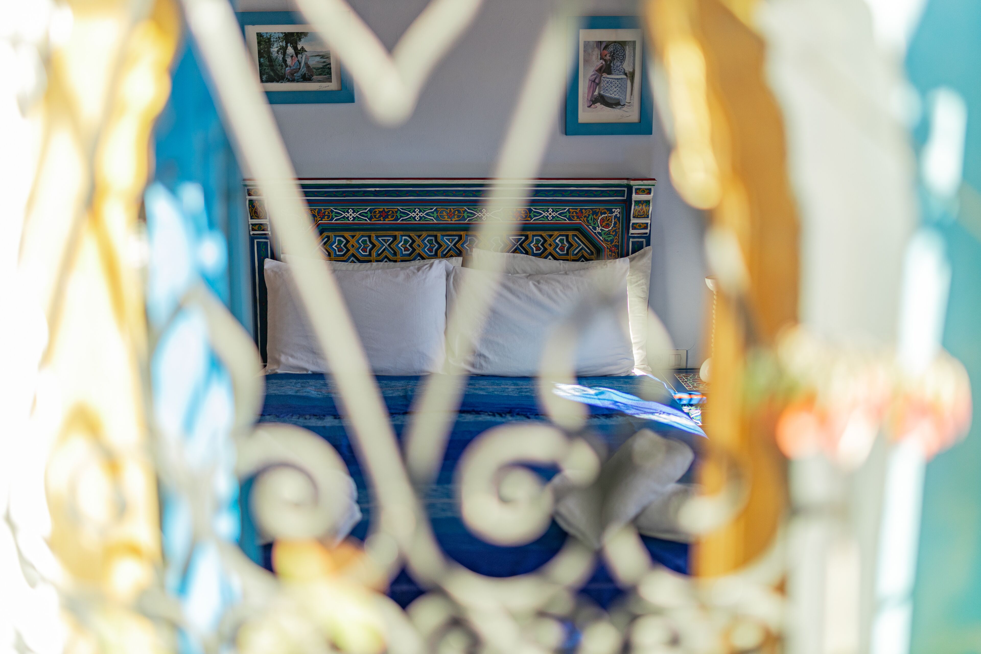 Uma cama com cabeceira estampada, almofadas brancas e colcha azul.