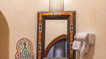 Un baño con un espejo decorativo, un secador de pelo e iluminación empotrada en la pared.
