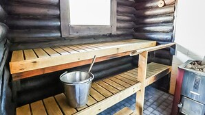 A rustic cabin interior with a wooden table, a metal bucket, and a window.