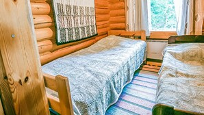 A cabin room with two beds, a window with curtains, and a log wall.