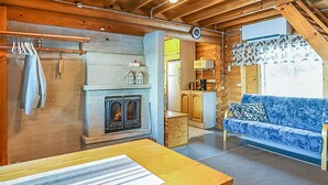 A cozy cabin interior with a fireplace, wooden walls, a sofa, and a dining area.