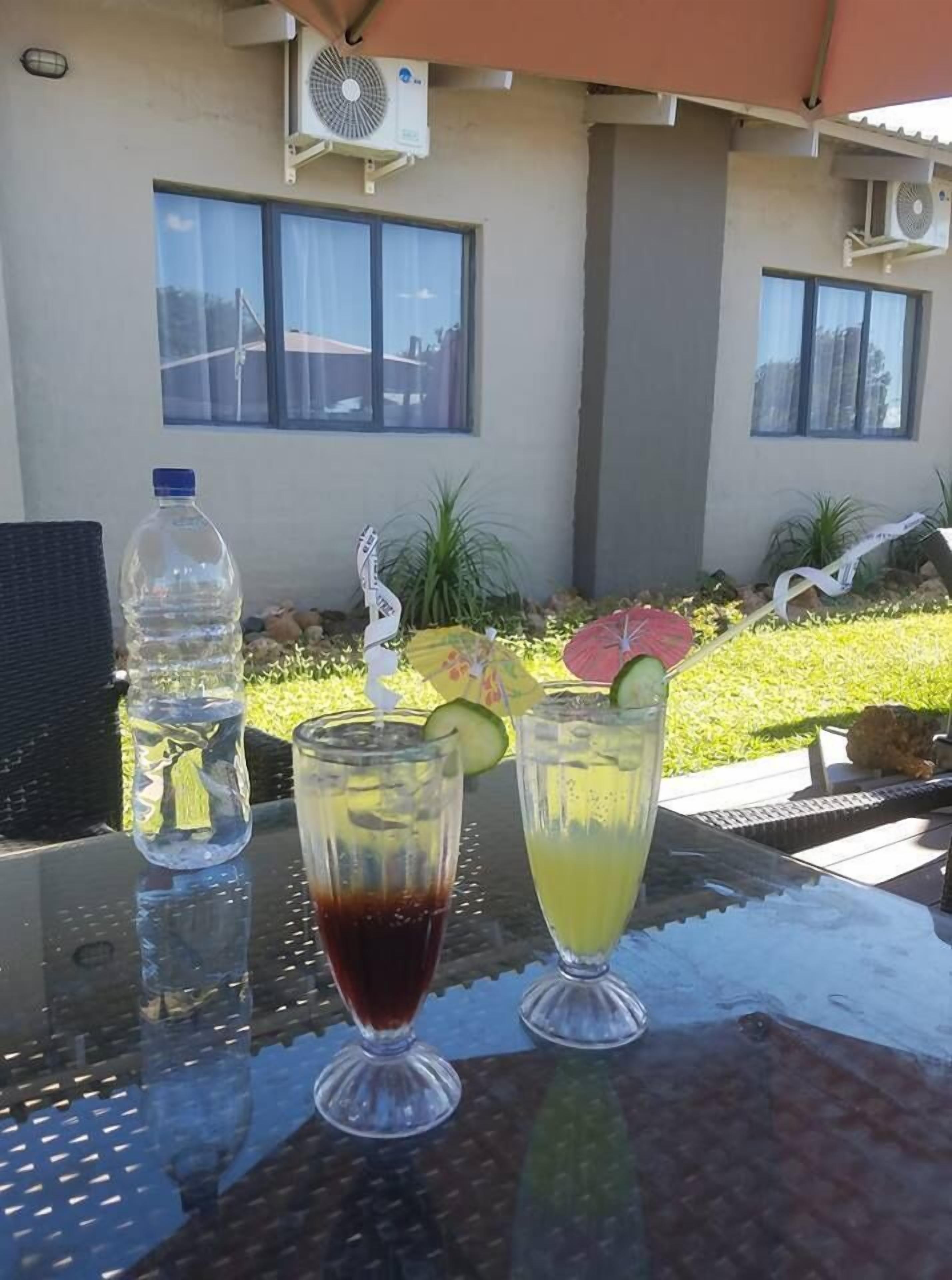 Mesa al aire libre con dos bebidas, una botella de agua y un paraguas decorativo.