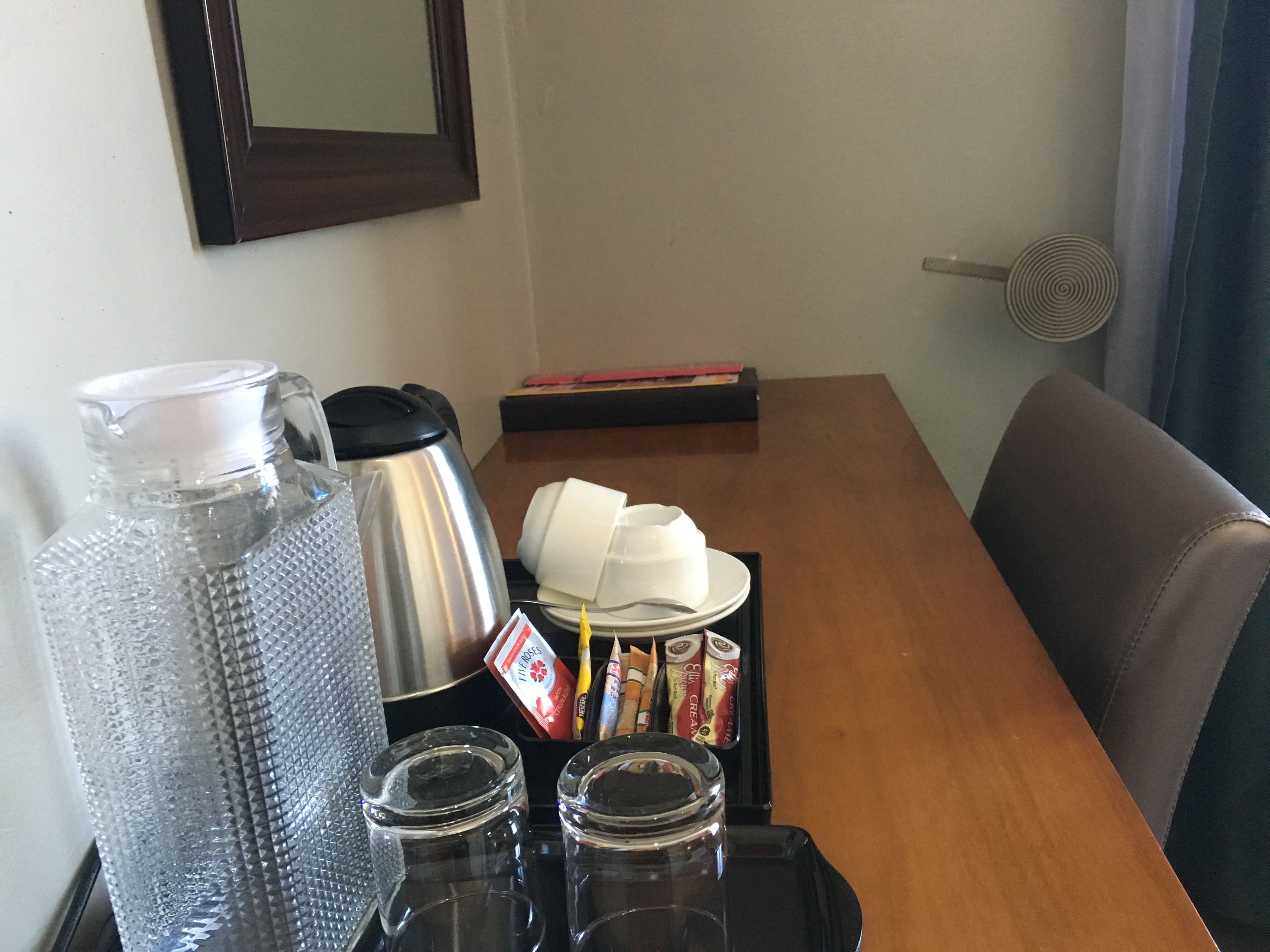 Una estación de café con cafetera, jarra, tazas y condimentos sobre una bandeja.