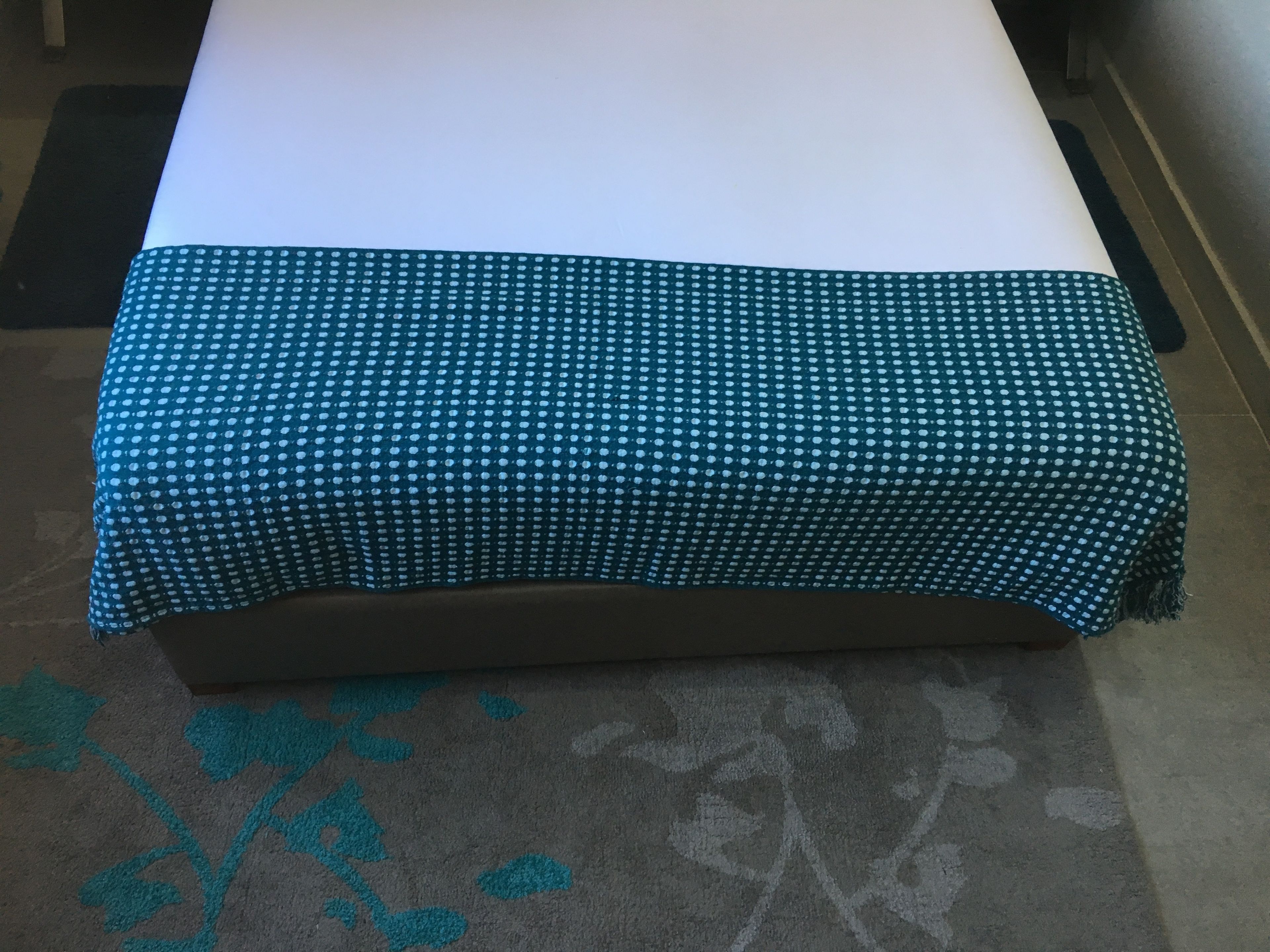 A bed with a teal polka dot bedspread and a floral-patterned rug.