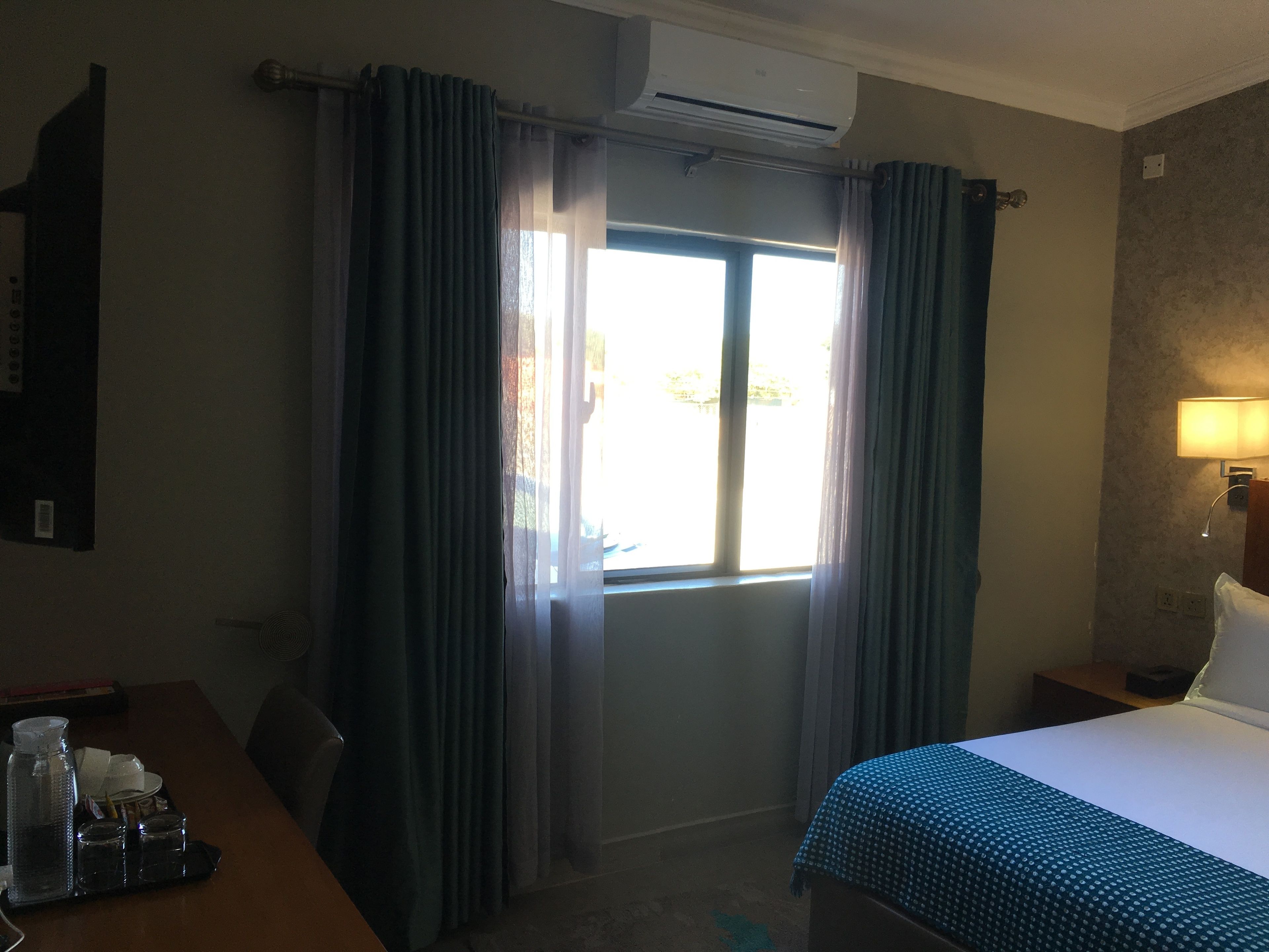 A hotel room with a bed, a desk with a lamp, and a window with curtains.