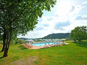 Un espace piscine agrémenté de chaises longues et de parasols, entouré d’arbres et offrant une vue sur les collines.