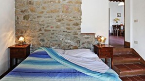 Ein Schlafzimmer mit Steinsturz, einem Bett mit blau-weißem Farbverlauf auf der Bettdecke, zwei Nachttischlampen und einer Treppe, die in einen Essbereich führt.