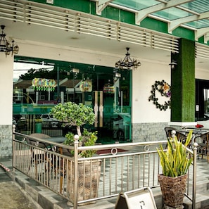 A hotel entrance with a glass facade, outdoor seating, and a green wall with a wreath.