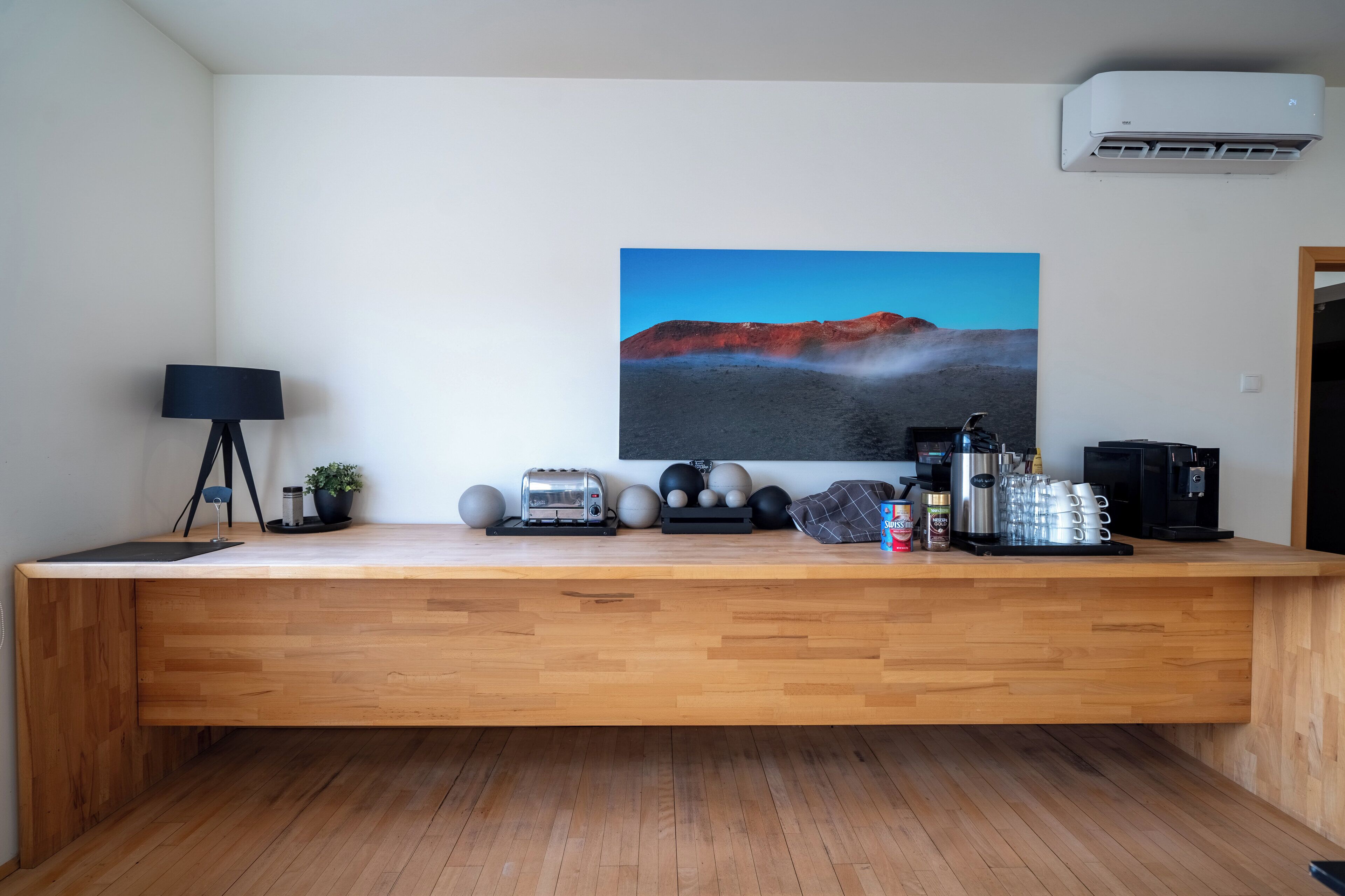 A modern kitchen with a wooden countertop, a toaster, coffee maker, and a painting of a volcanic landscape.