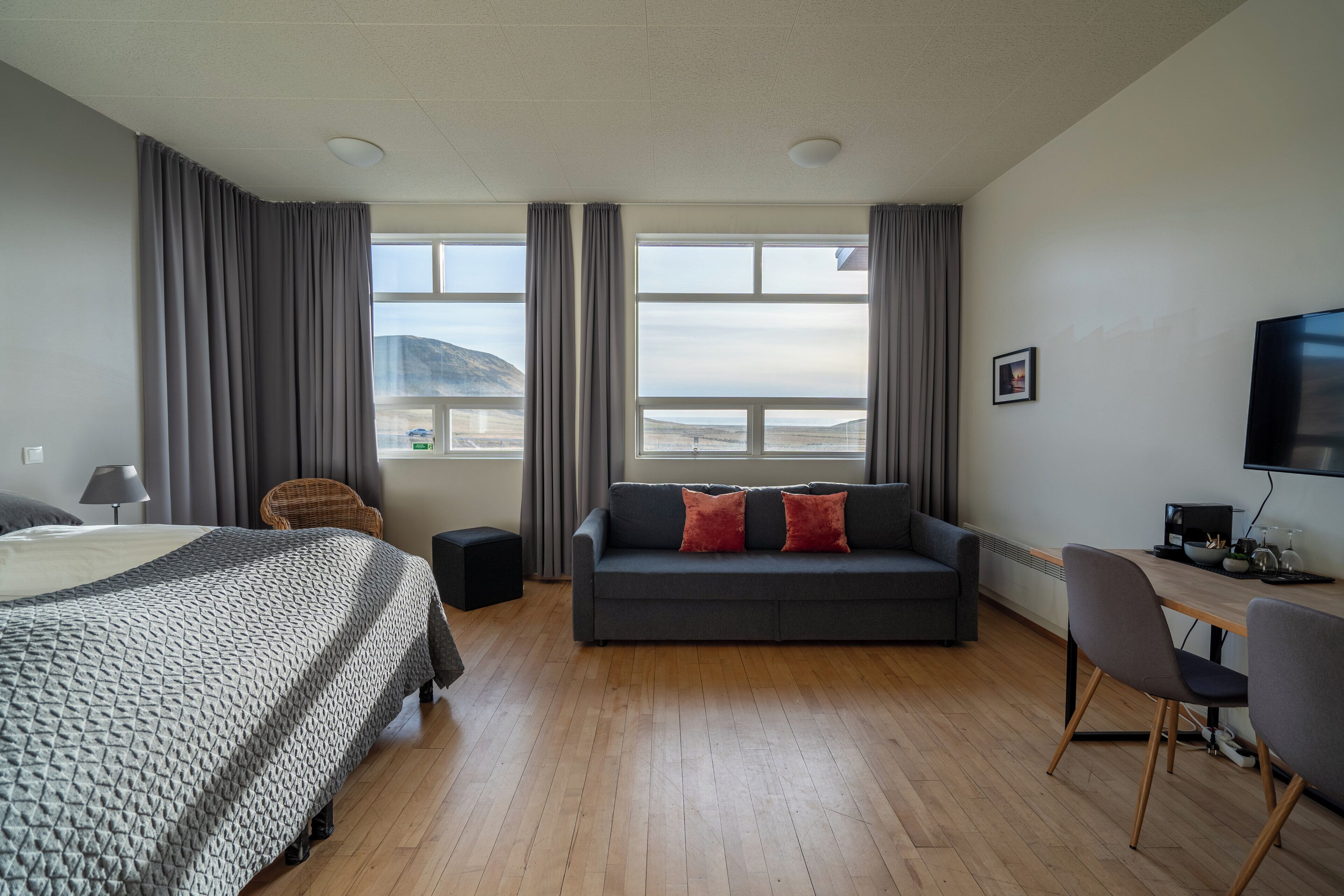 Una habitación de hotel con cama, sofá, escritorio con televisor y vista a las montañas.