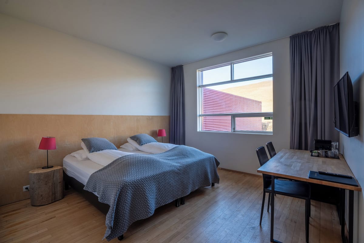 A hotel room with two beds, a dining table, a TV, and a window with curtains.