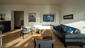 A modern living room with a wooden coffee table, a black leather sofa, and a grey armchair.