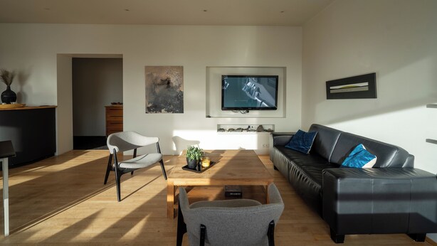 Una sala de estar moderna con una mesa de centro de madera, un sofá de cuero negro y un sillón gris.