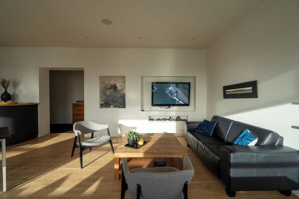 A modern living room with a wooden coffee table, a black leather sofa, and a grey armchair. - Volcano hotel (Vik I Myrdal)