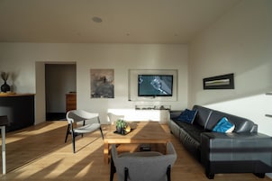 Una sala de estar moderna con una mesa de centro de madera, un sofá de cuero negro y un sillón gris.