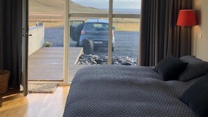 Un dormitorio con una cama grande, una lámpara roja y vista a un coche estacionado a través de un ventanal.