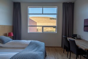 Habitación de hotel con cama, escritorio y vista a un campo a través de un gran ventanal.