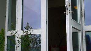 Fachada de un edificio con puerta blanca y ventanas amplias. Hay plantas en macetas afuera y un felpudo en la entrada.