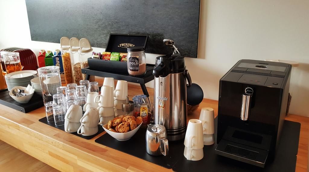 Una barra de desayuno con máquinas de café, tazas y un bol de galletas.