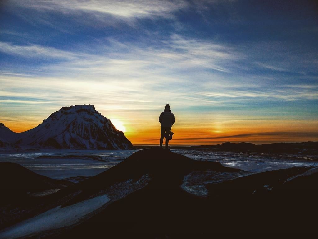 Una persona de pie sobre una roca con una montaña al fondo durante el atardecer.