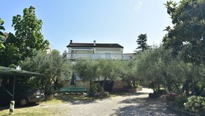 Uma casa grande com jardim, um carro e um banco.