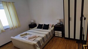 Quarto com cama, mesas de cabeceira, um guarda-roupa e janela com cortinas.