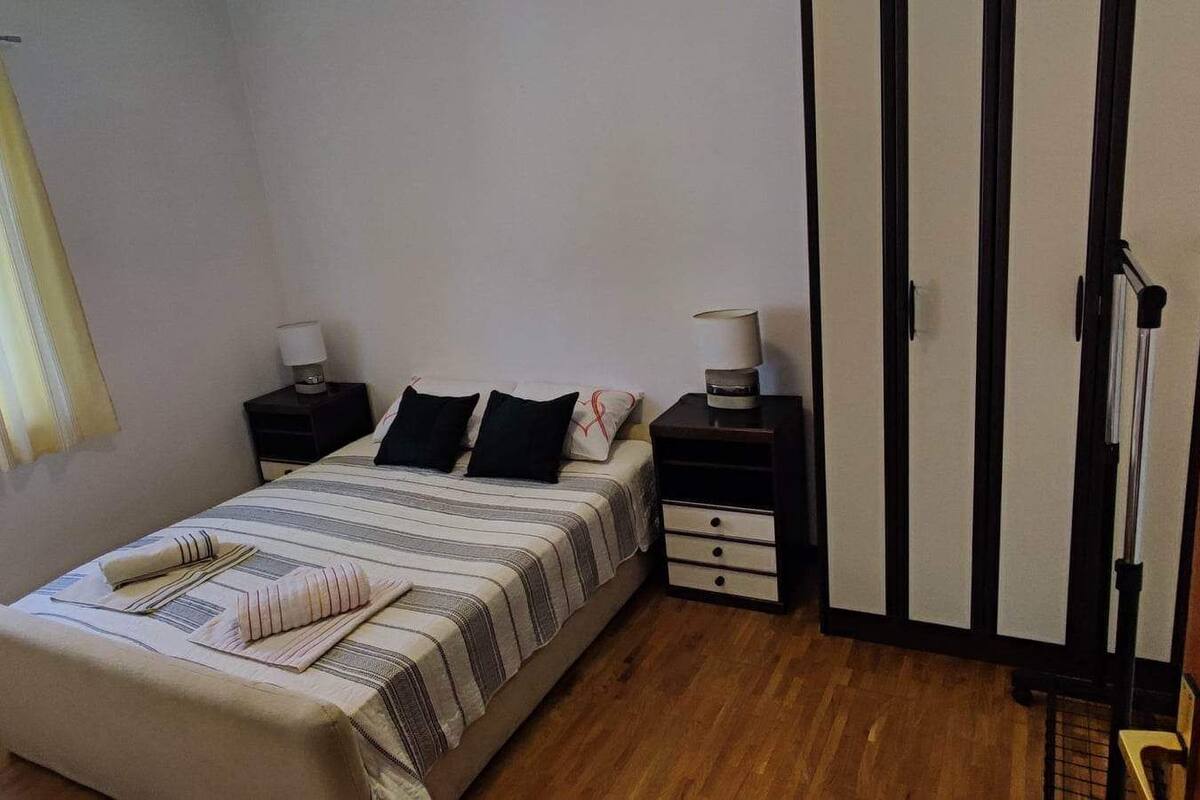 A bedroom with a bed, bedside tables, a nightstand, a wardrobe, and a window with curtains.
