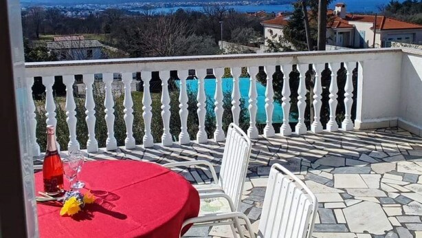 Um pátio com mesa vermelha e cadeiras brancas, com vista para uma paisagem deslumbrante montanhas e um corpo d'água.