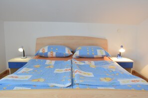 Una cama con un edredón azul estampado con flores, dos almohadas iguales y dos lámparas de noche sobre mesitas de madera.