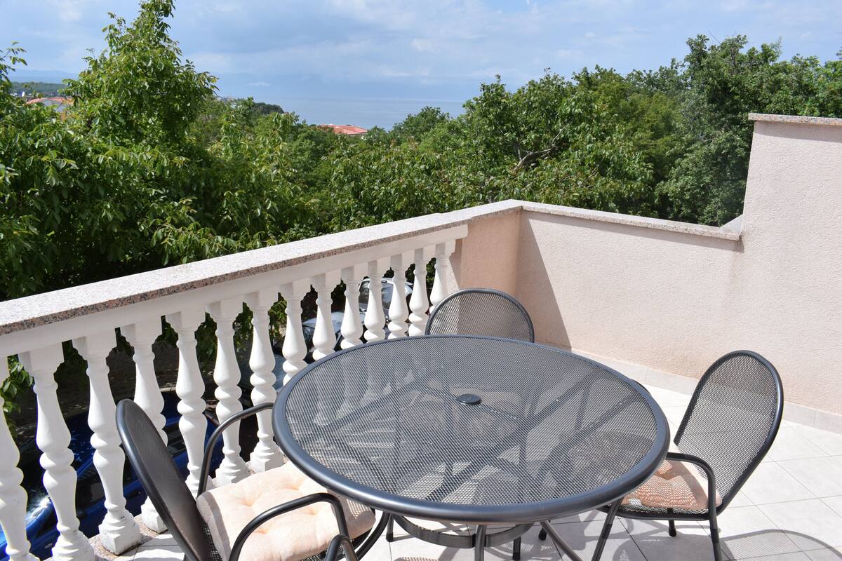 A balcony with a round metal table and two chairs, surrounded by a white balustrade.