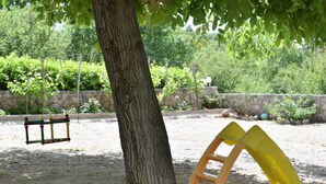 Une aire de jeux avec des balançoires, un toboggan et un arbre au centre.