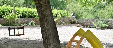 A playground with a swing set, a slide, and a tree in the center.