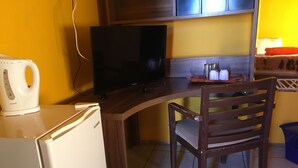 Ett litet kök med ett kylskåp, en tv, en trästol och en vattenkokare.