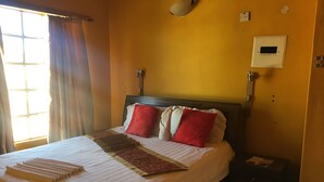 Ett hotellrum med en säng, ett nattduksbord, en väggmonterad lampa och ett fönster med gardiner.
