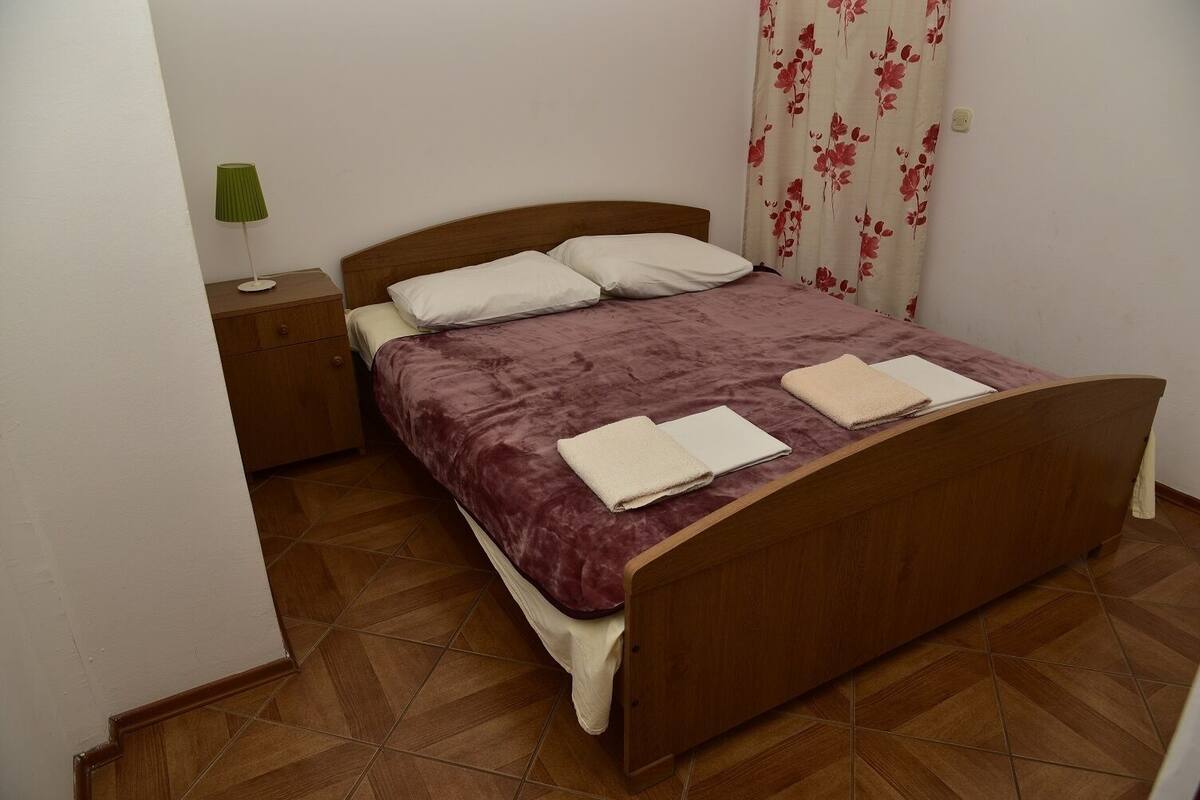 Un lit simple avec un cadre en bois et une couvre-lit violette, deux oreillers blancs et deux serviettes pliées posées sur le lit.