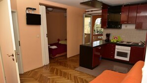 A compact kitchen with a herringbone floor, a small dining area, and a bedroom with a bed and a nightstand.