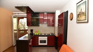 A compact kitchen with red cabinets, a stove, and a sink. There is a dining area with a chair and a table.