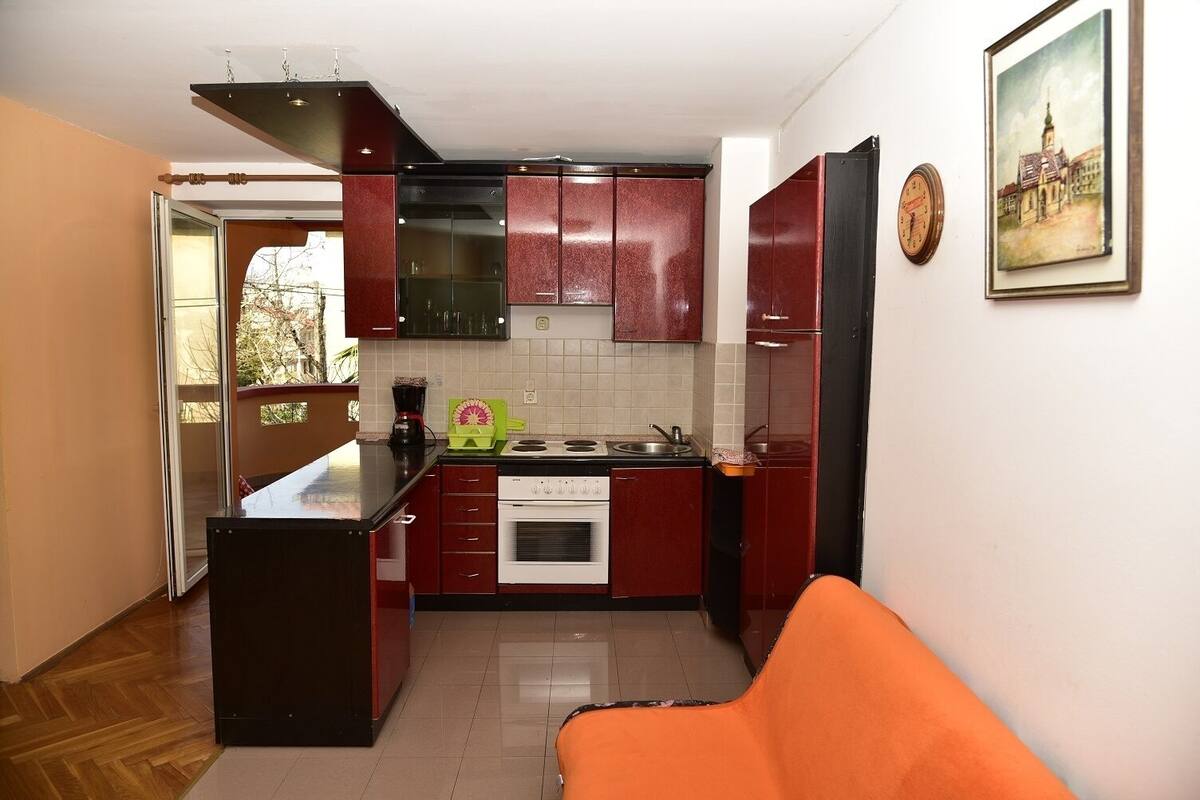 Une cuisine compacte avec des meubles rouges, une cuisinière et un évier. On y trouve également un coin repas avec une chaise et une table.