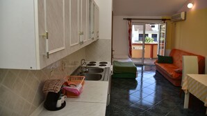 A compact kitchen with a sink, stove, and cabinets. A dining area with a sofa and a table is visible in the background.