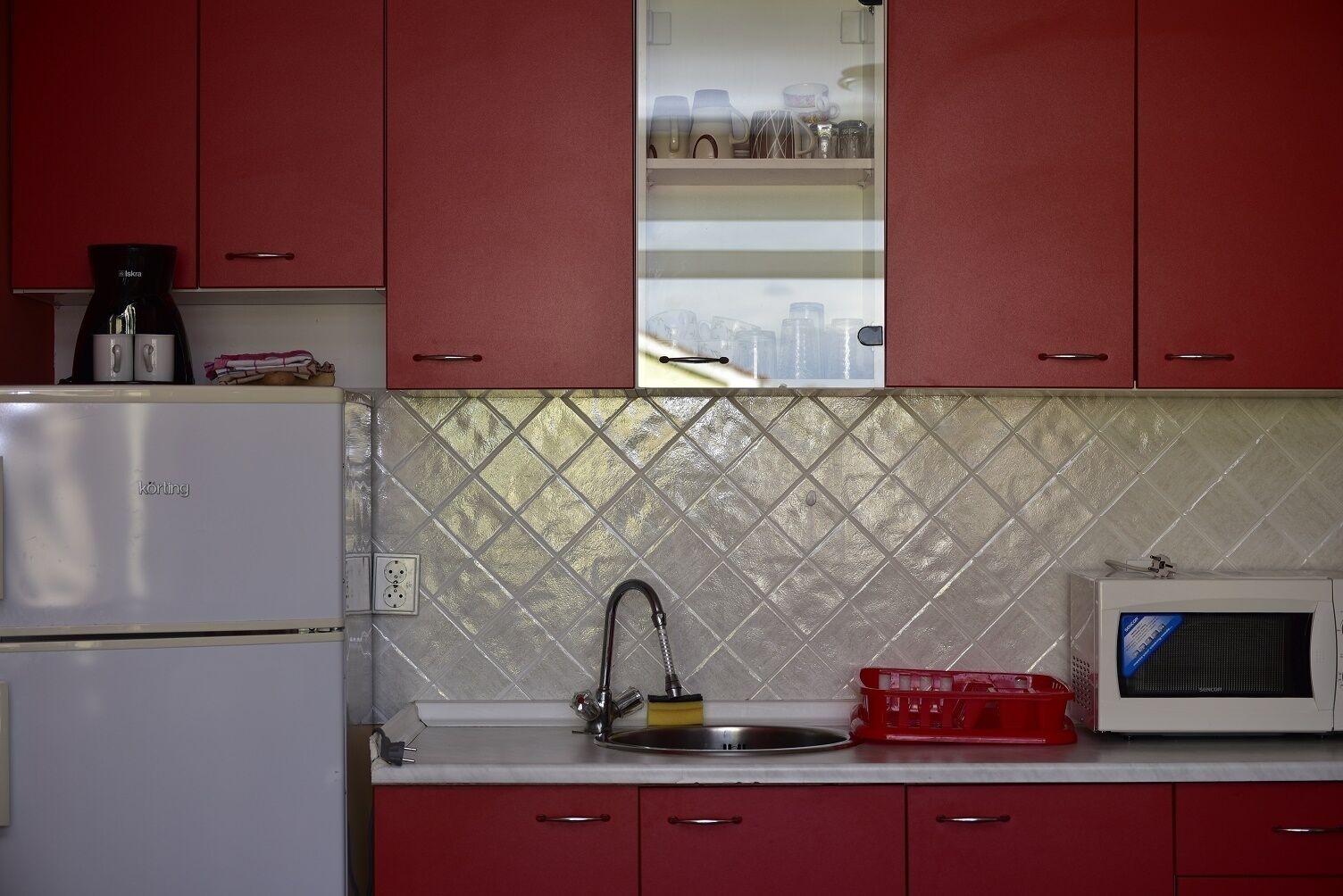 A kitchen with red cabinets, a white refrigerator, a sink with a faucet, and a microwave.