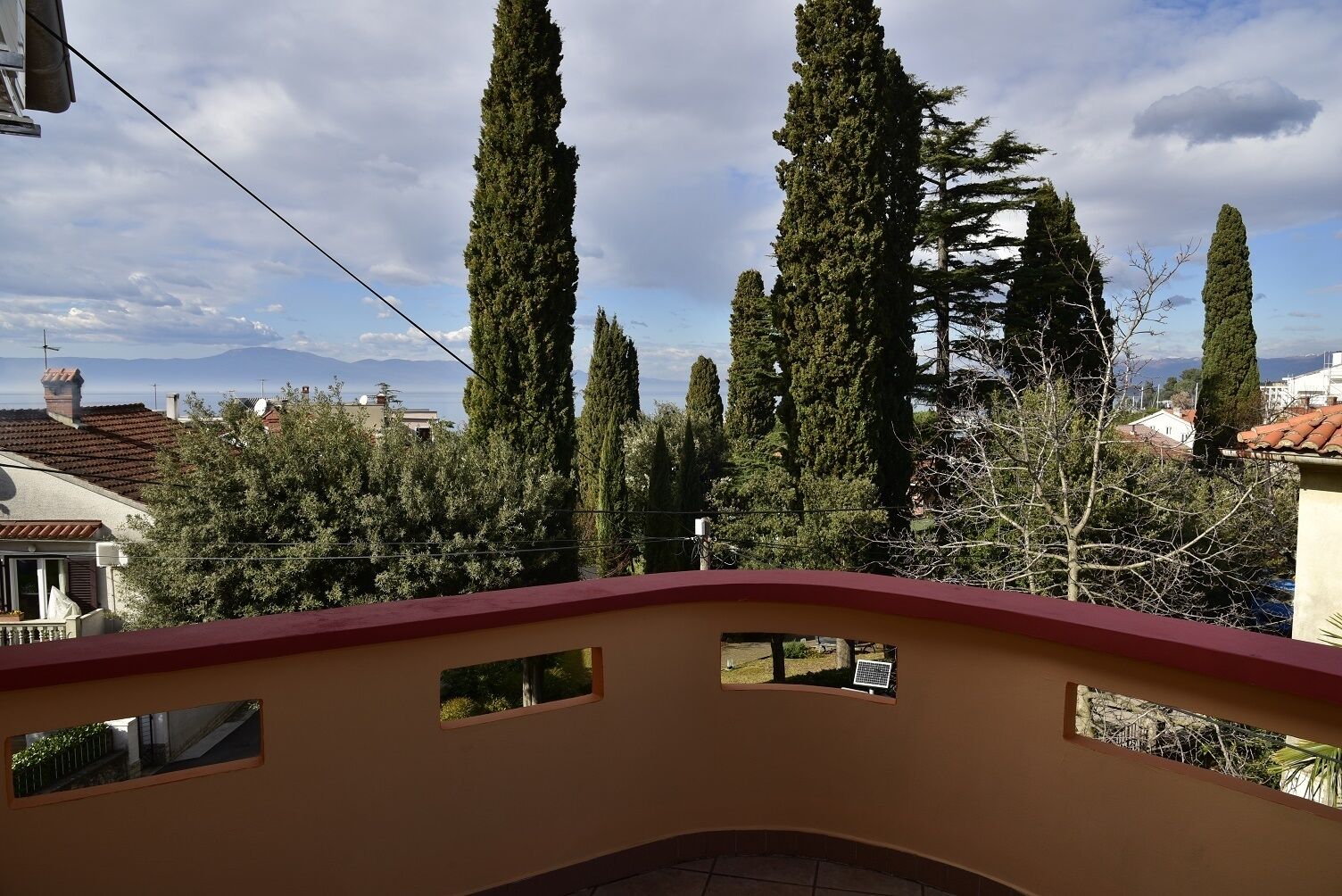 A balcony with a view of tall cypress trees and distant mountains.