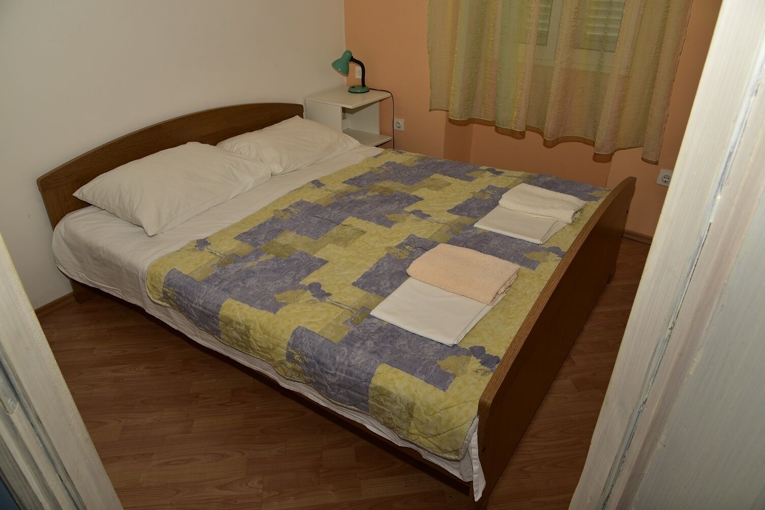 Ein Einzelbett mit einer Steppdecke, ein Nachttisch mit Lampe und ein Fenster mit Vorhängen.