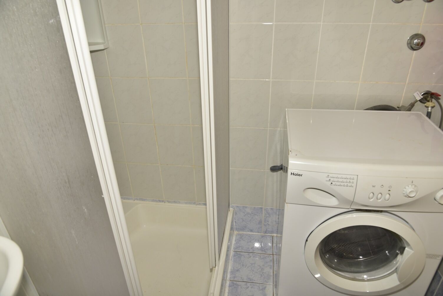 Ein Waschraum mit einer Frontlader-Waschmaschine und einer Dusche.