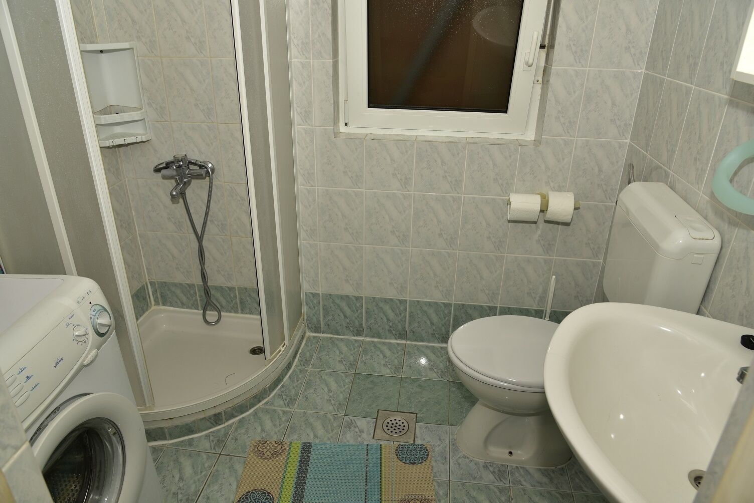 A bathroom with a shower, toilet, sink, and washing machine.