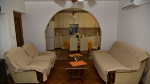 A living room with two sofas, a dining table with chairs, and an arched kitchen in the background.