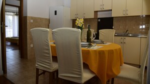 A dining area with a yellow tablecloth, four chairs, a vase with flowers, and a refrigerator in the background.