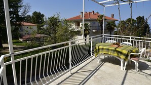 A balcony with a table and chairs, a white railing, and a view of a house with a red roof.