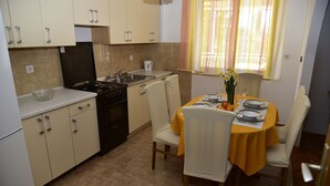 A compact kitchen with a stove, sink, and cabinets. There is a dining table with chairs and a yellow tablecloth.