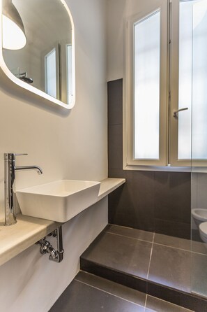 A modern bathroom with a white sink, a mirror, and a window. - Appartamento Matteotti (Bologna)
